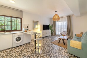 A compact living space with a kitchen, dining area, and seating area, featuring a patterned floor, a washing machine, a television, and a large window. - Casa Castillo | Orange Square Apartment (Marbella)