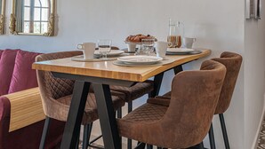 Ein Essbereich mit einem Holztisch, braunen Polsterstühlen, einem weißen Teller, einer Glasgießkanne und einer Muffin-Form.