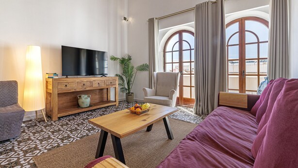 Ein Wohnzimmer mit Fernseher, Sofa, Sessel und einem Couchtisch mit Früchten.