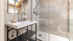 Ein Badezimmer mit Duschkabine aus Glas, einem weißen Waschbecken und einem Spiegel darüber.