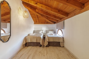 Une chambre avec deux lits, des poutres apparentes en bois au plafond, un luminaire suspendu et un grand miroir.