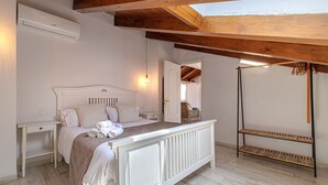 Ein Schlafzimmer mit einem weißen Bett, einem Nachttisch, einem Holzboden und einem Deckenventilator.