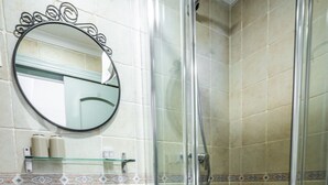 A bathroom with a white pedestal sink, a glass shower enclosure, and a mirror with a decorative frame.