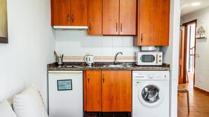 A compact kitchen with wooden cabinets, a microwave, a washing machine, and a small sink.