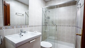 Et badeværelse med hvid vask, toilet og brusekabine med glasvægge.