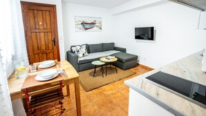 En kompakt opholdsstue med spiseplads, sofa, tv og tekøkken.