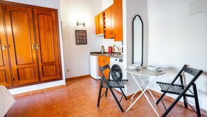 A compact kitchen with wooden cabinets, a washing machine, and a dining area with two chairs and a small table.