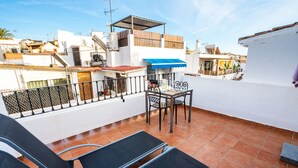 A rooftop terrace with two lounge chairs, a table, and a blue awning.