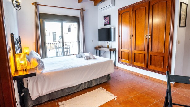 A bedroom with a bed, a TV, a wardrobe, and a balcony view.