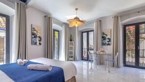 A modern hotel room with a large bed, a dining area, and a balcony with a view.