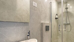 A modern bathroom with a large white sink, a toilet, and a glass-enclosed shower area.