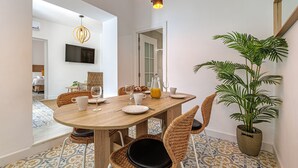 A dining area with a wooden table, wicker chairs, a potted plant, and a TV mounted on the wall. - Casa Serena  | Family Apartment (Marbella)