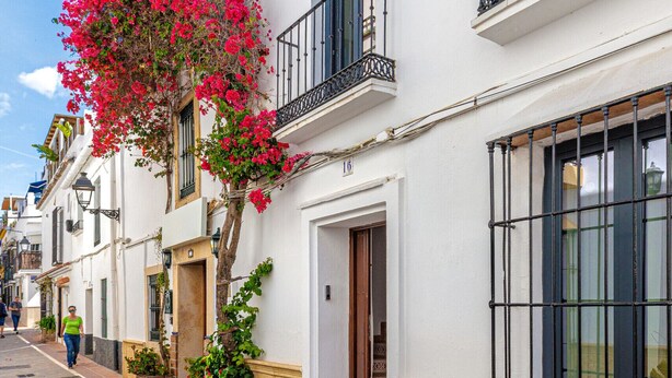 A street with white buildings, a tree with pink flowers, and a clear blue sky. - Casa Serena  | Family Apartment (Marbella)