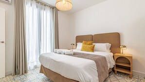 A hotel room with a bed, a nightstand, a lamp, and a patterned floor. - Casa Serena  | Family Apartment (Marbella)