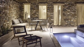 Et rum med stenvægge, en swimmingpool, et spisebord med stole og en sofa.