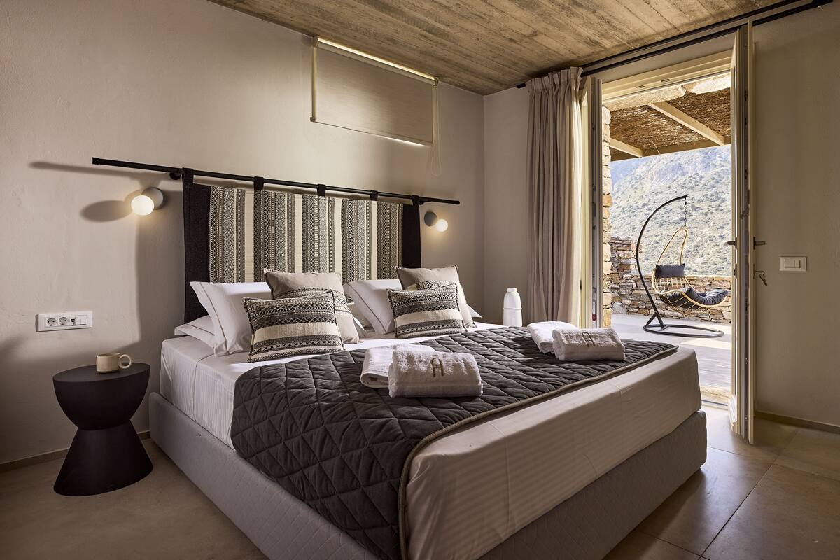 Un dormitorio con una cama grande, una mesita de noche, una lámpara colgante y vistas al exterior.
