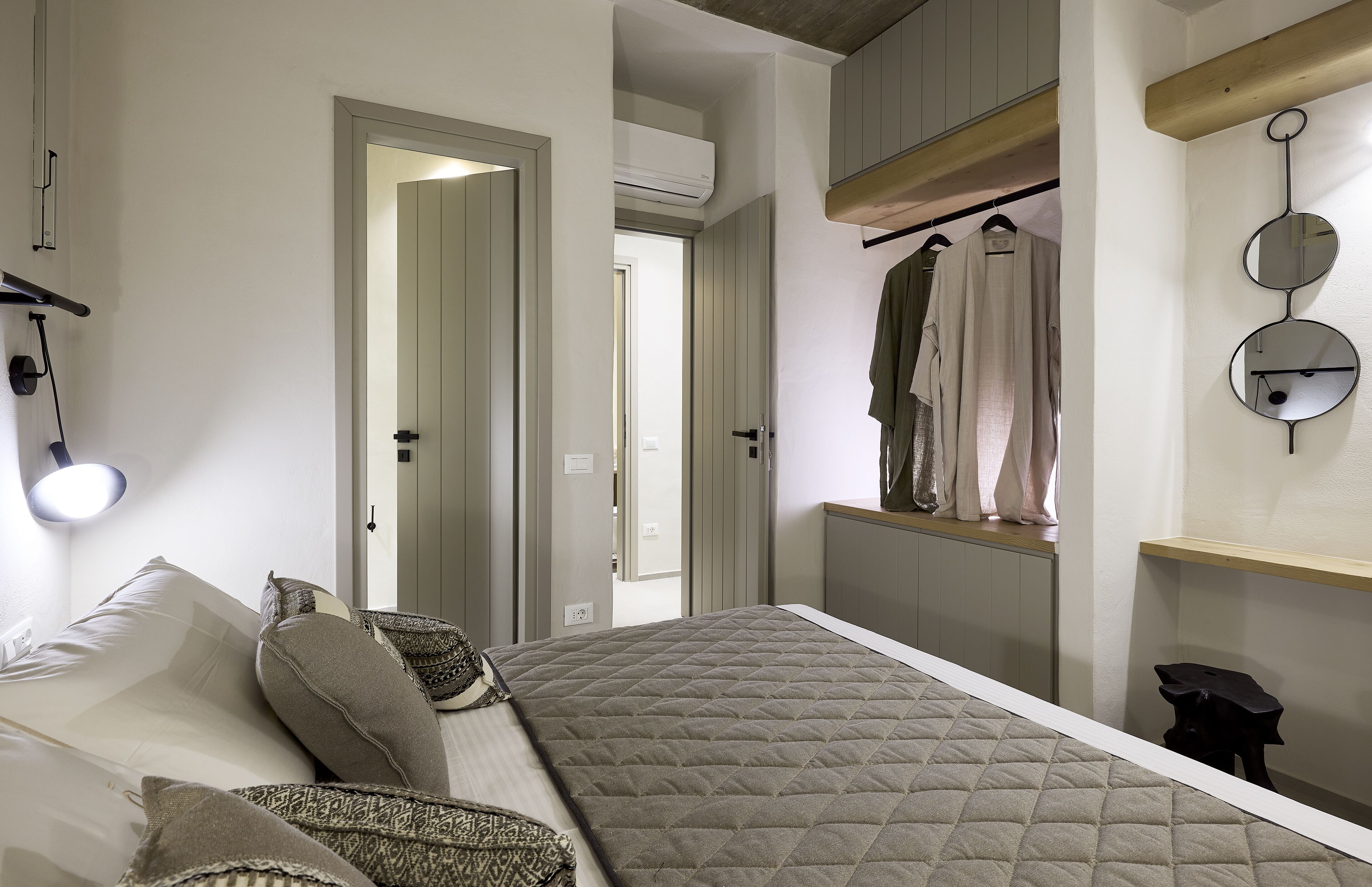 Ein Schlafzimmer mit Bett, Kissen, Nachttischlampe, Spiegel und einer Garderobe.
