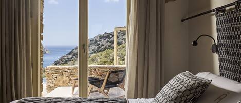 A bedroom with a bed, a view of the sea, and a stone wall.