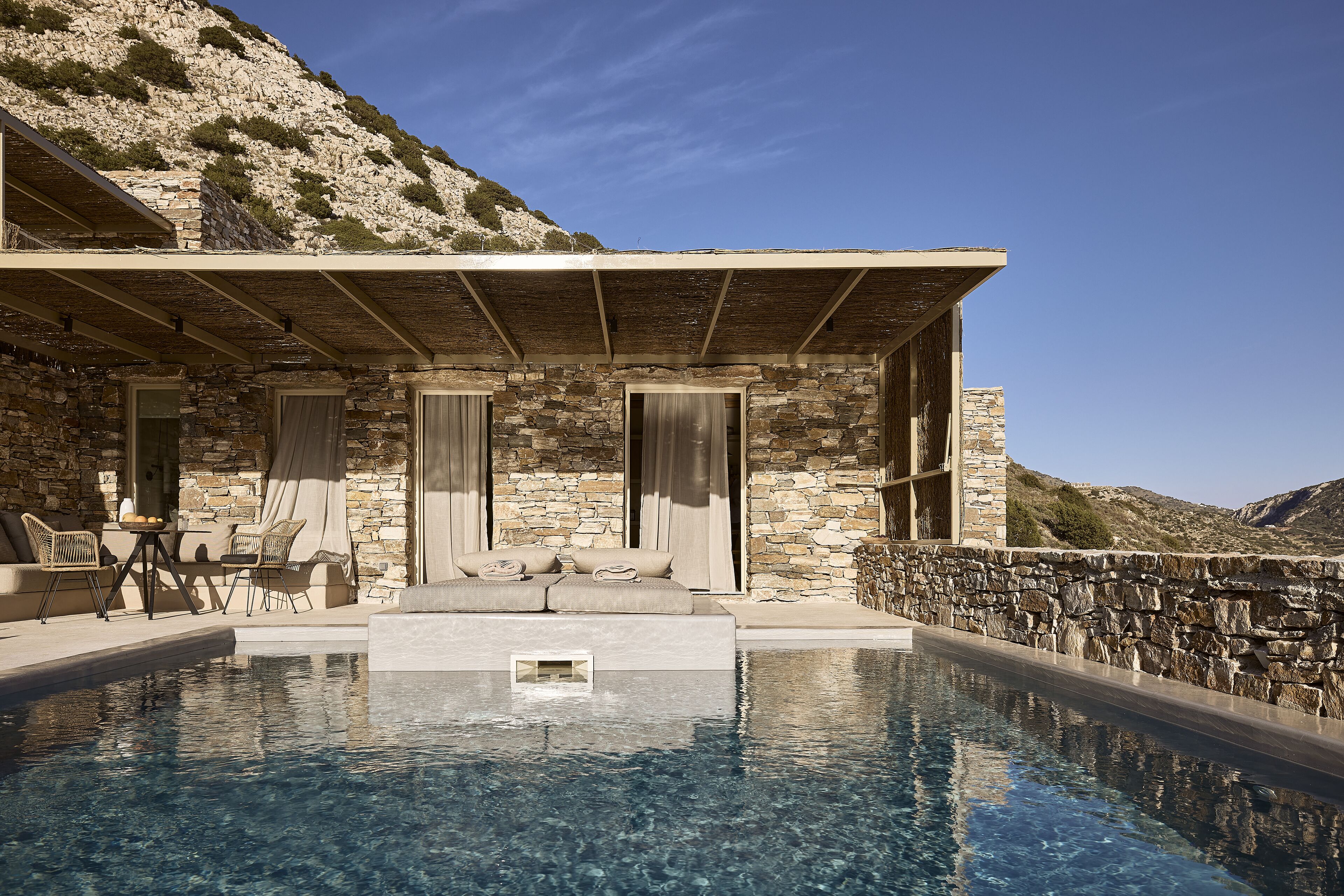 A poolside area with stone walls, a covered seating area, and a view of the mountains.