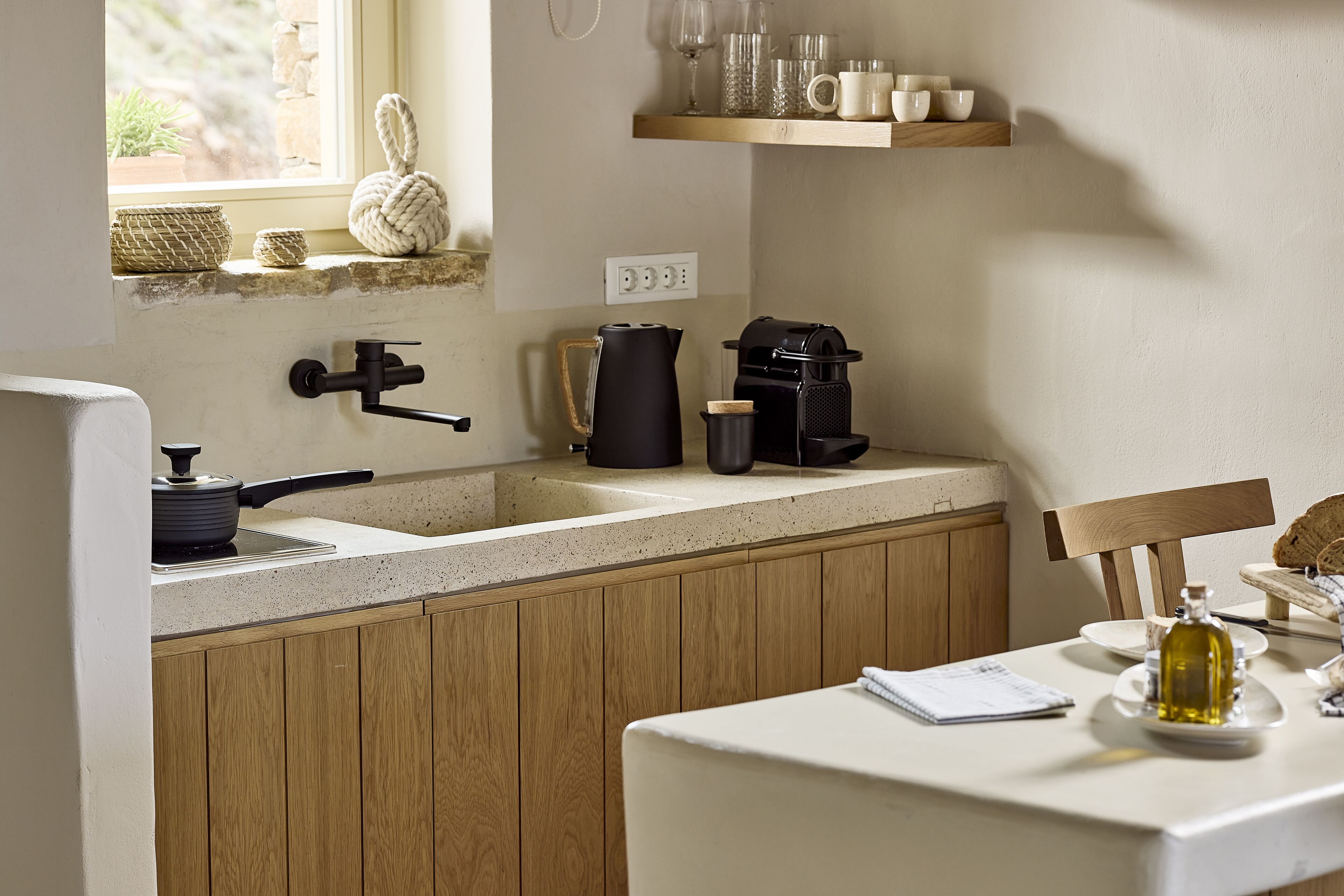 A kitchen with wooden cabinets, a sink, a coffee maker, and a window with a view of greenery.