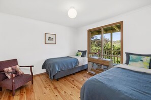 A bedroom with two beds, a chair, a desk, and a window with a view of trees. - Green Gully House (Aireys Inlet)