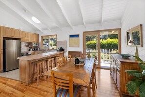 A modern kitchen with wooden cabinets, a stainless steel refrigerator, and a large island with bar stools. - Green Gully House (Aireys Inlet)