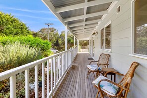 A covered wooden deck with white railings, two wicker chairs with cushions, and a view of a lush garden. - Green Gully House (Aireys Inlet)