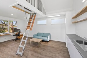 A modern interior with a loft bedroom, a kitchen, and a living area. - Green Gully House (Aireys Inlet)