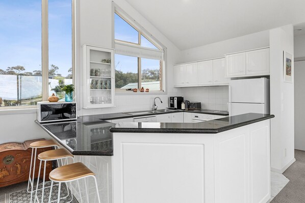 A modern kitchen with white cabinetry, a black countertop, and a large window.