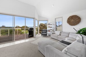 A modern living room with a grey sofa, a bookshelf, and a large window offering a view of the outdoors.