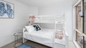 Ein Schlafzimmer mit Etagenbett, einem kleinen runden Tisch und einem blau gemusterten Teppich.