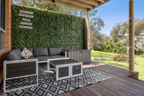 Ein Sitzbereich im Freien mit einer Couch, einem Couchtisch und Beistelltischen, einem an der Wand befestigten Schild mit Ortsnamen und einer Holzterrasse.