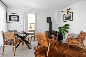 A room with a round table, two chairs, a sofa, a fireplace, a plant, and artwork on the walls.