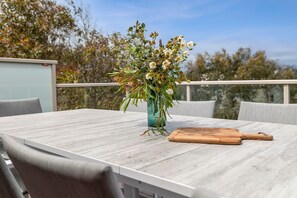 A dining table with a vase of flowers, a wooden cutting board, and outdoor seating. - Gumnut House (Anglesea)