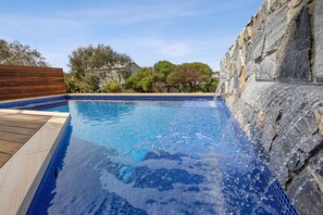 A swimming pool with a wooden deck and stone walls.