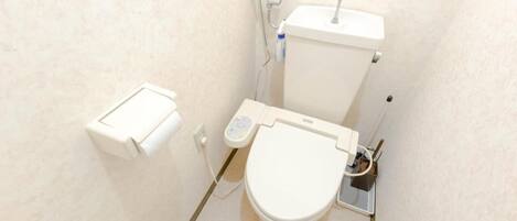 A small, compact bathroom with a toilet, a bidet, and a toilet paper holder.