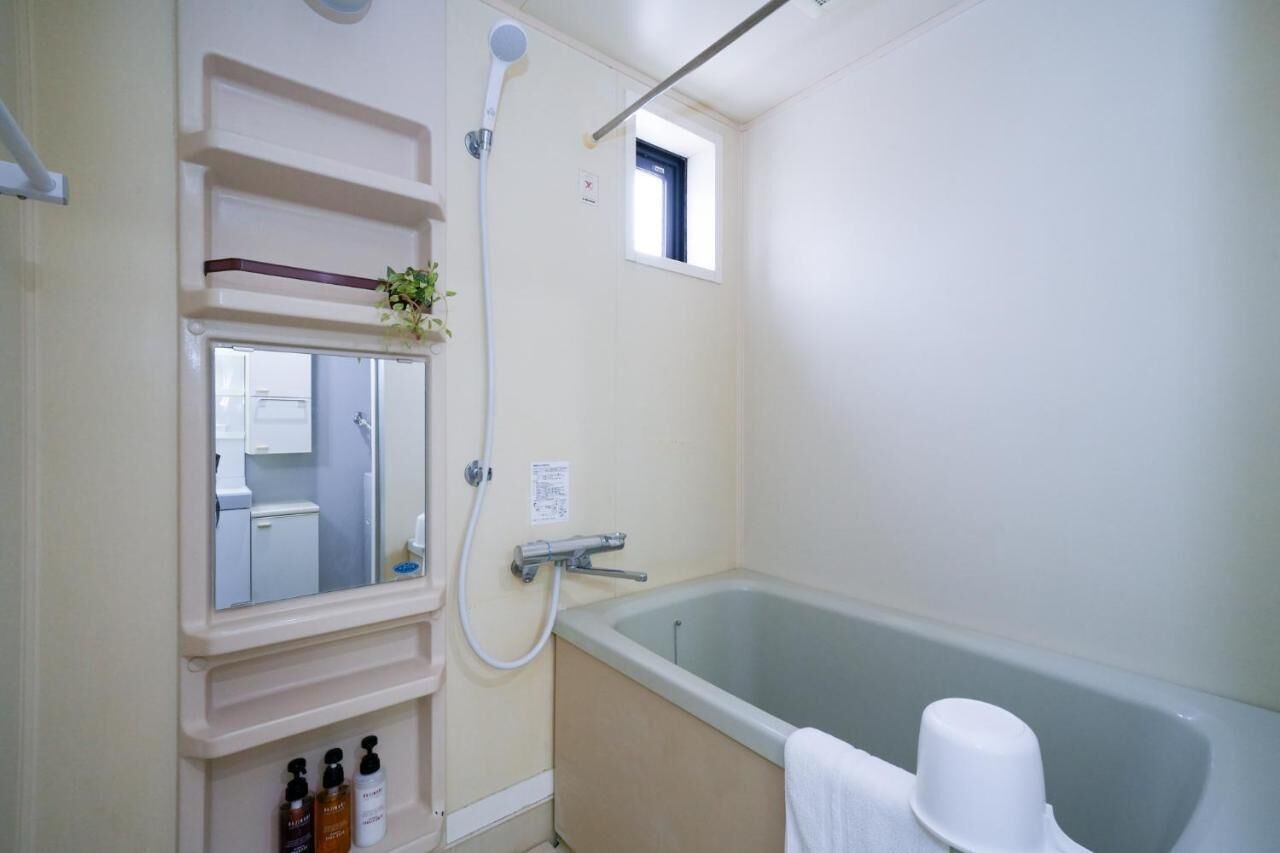 A bathroom with a bathtub, a shower, a mirror, and a small window.
