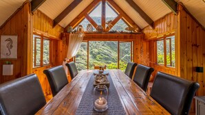 Comedor de madera con techo alto y ventanas amplias que dan a un bosque.