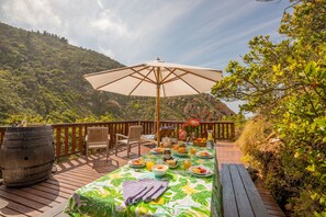 A wooden deck with a table set for breakfast, surrounded by chairs, a large umbrella, and a rustic barrel. - Ballots Bay Treehouse by HostAgents   (George)
