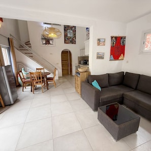 Un salon comprenant un canapé, une table basse, une table à manger avec des chaises et un escalier.