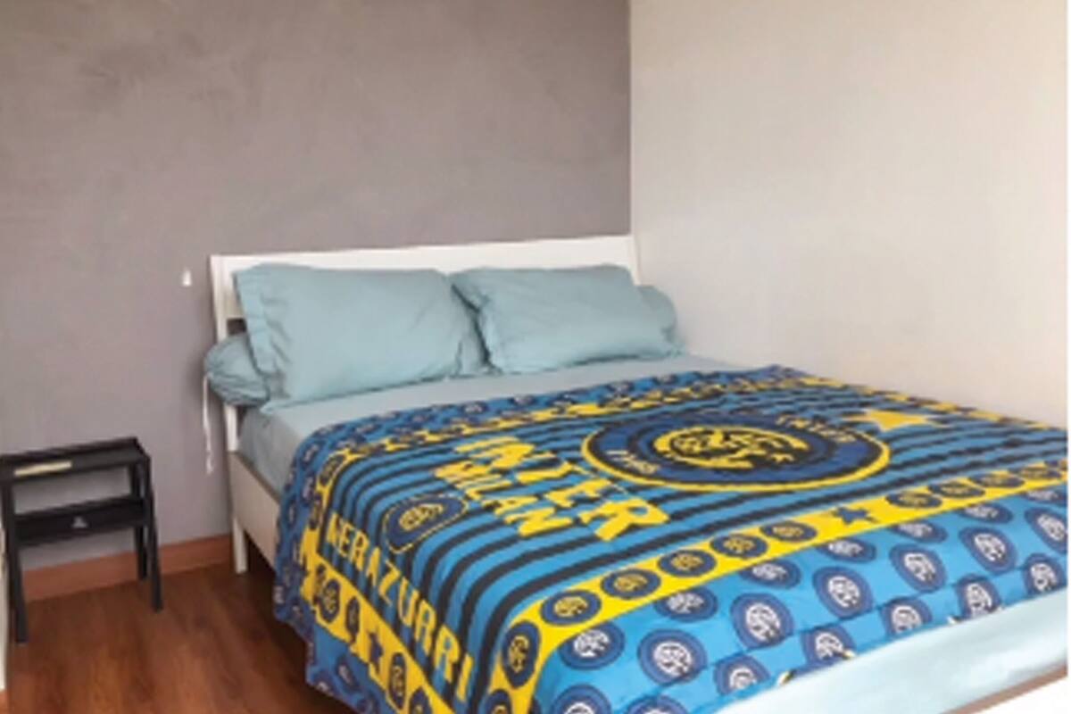 Ein Schlafzimmer mit einem Bett, zwei Kissen, einem Nachttisch und einer gemusterten Bettdecke.