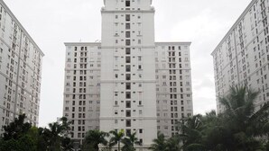 A high-rise building with multiple floors, surrounded by palm trees and a swimming pool.