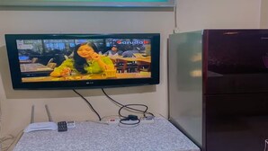 A television mounted on a wall displaying a show with a tropical background.