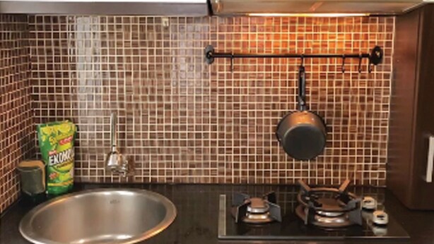 A kitchen with a stainless steel sink, a hanging pot rack, and a tiled backsplash.