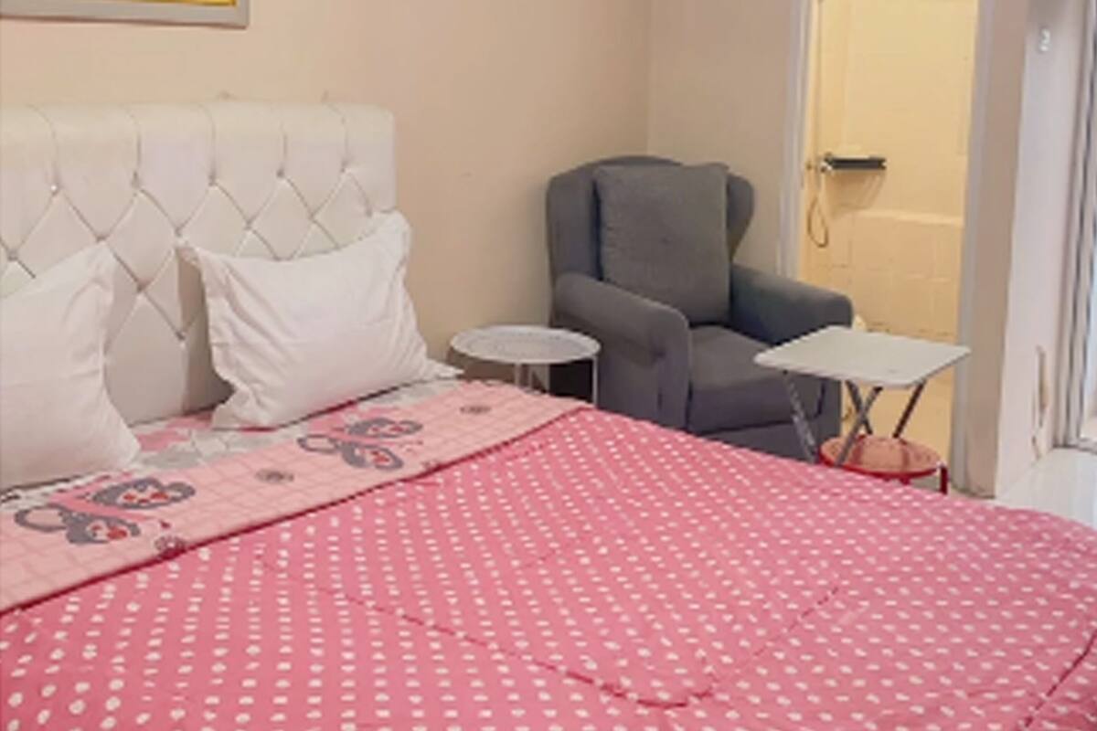 Ein Schlafzimmer mit einem Bett, einem grauen Sessel, einem kleinen runden Tisch und einem weißen Kopfteil.