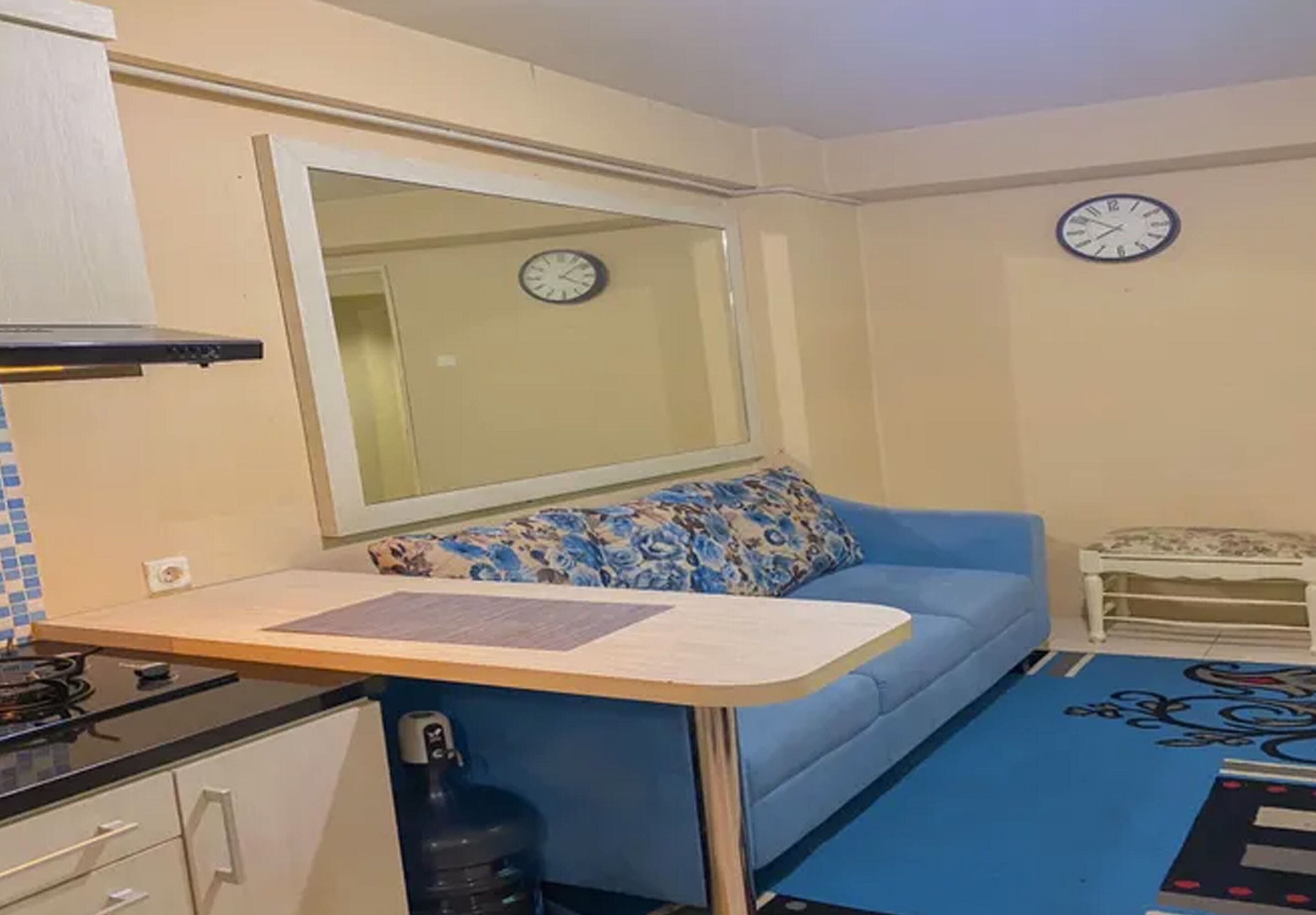 A compact living space with a kitchenette, a blue sofa with a floral cushion, a small table, and a decorative rug.