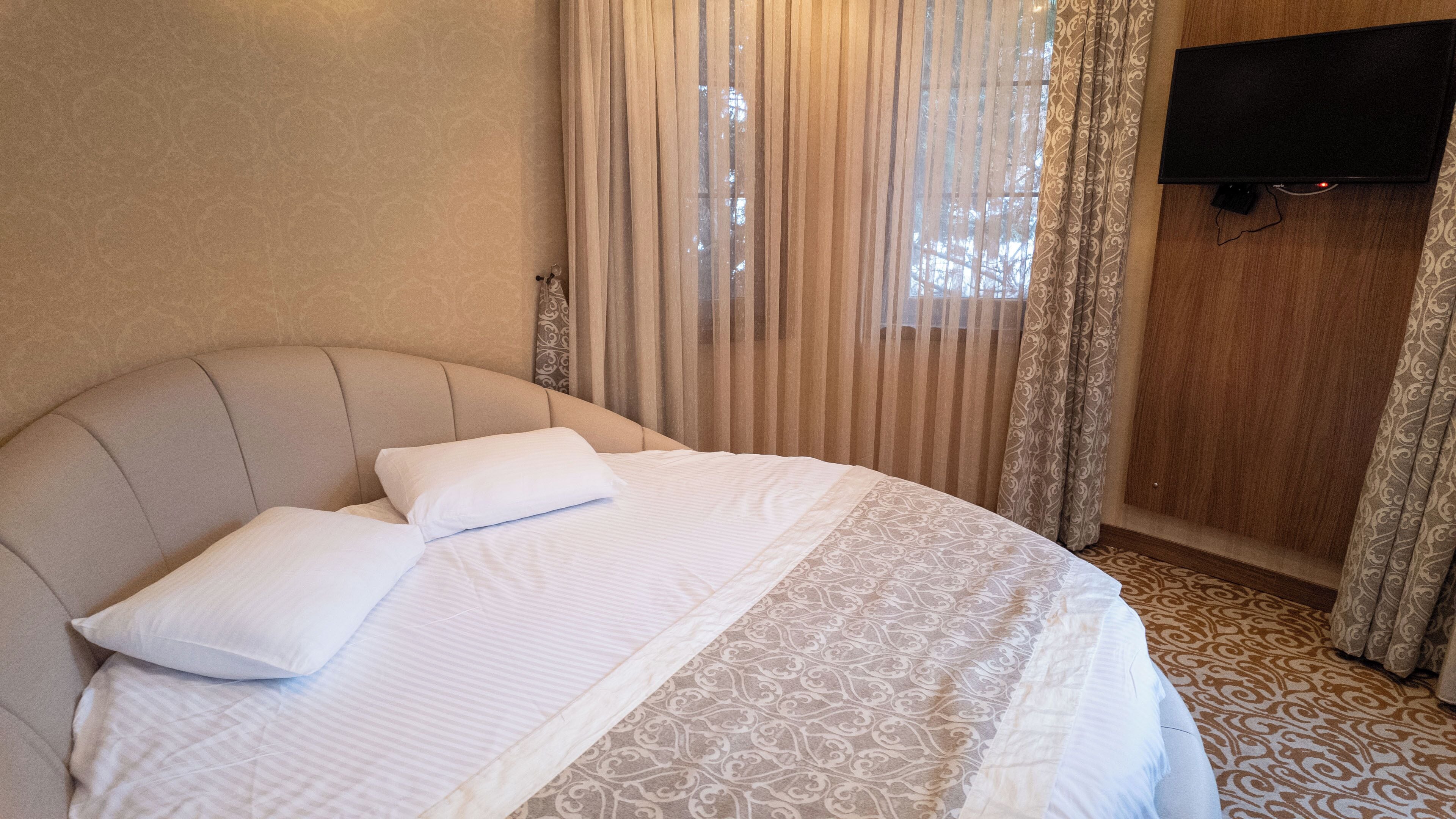 A neatly made bed with a headboard, white bedding, and a patterned area rug.