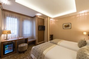 Quarto de hotel com duas camas, uma mesa de trabalho com luminária, televisão e um minibar.