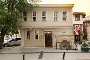 Um edifício de dois andares com fachada bege, uma entrada central com pequeno alpendre e uma lareira de pedra.