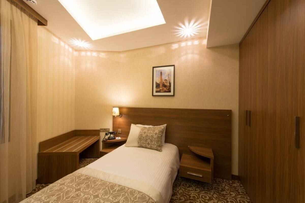 A hotel room with a large bed, a bedside table with a lamp, a nightstand, and a wardrobe.